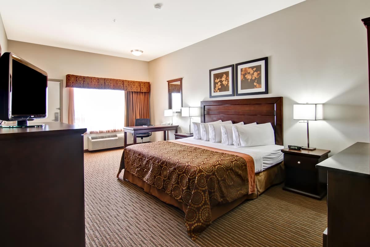 A hotel room with a large bed, a desk with a computer, a TV, and two bedside lamps.