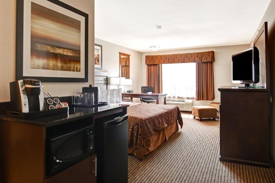 A hotel room with a bed, a desk, a television, a microwave, a coffee maker, and a window with curtains.