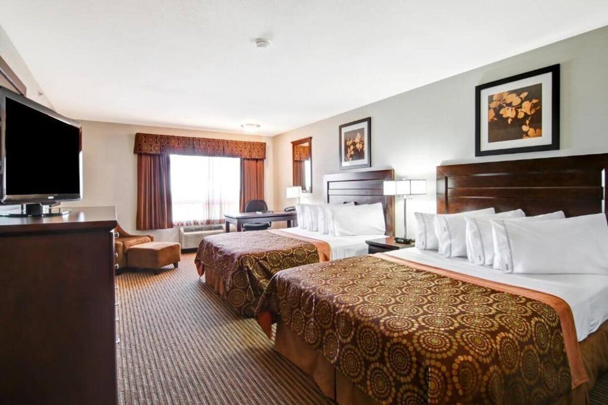 A hotel room with two beds, a desk, a TV, and a large window with curtains.