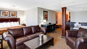 Une chambre d’hôtel avec un grand lit, un canapé en cuir marron, un bureau avec une chaise et une petite table.