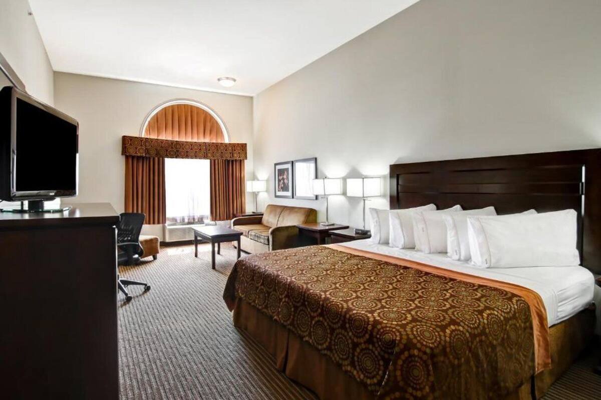 A hotel room with a large bed, a desk with a television, a sofa, and a window with curtains.