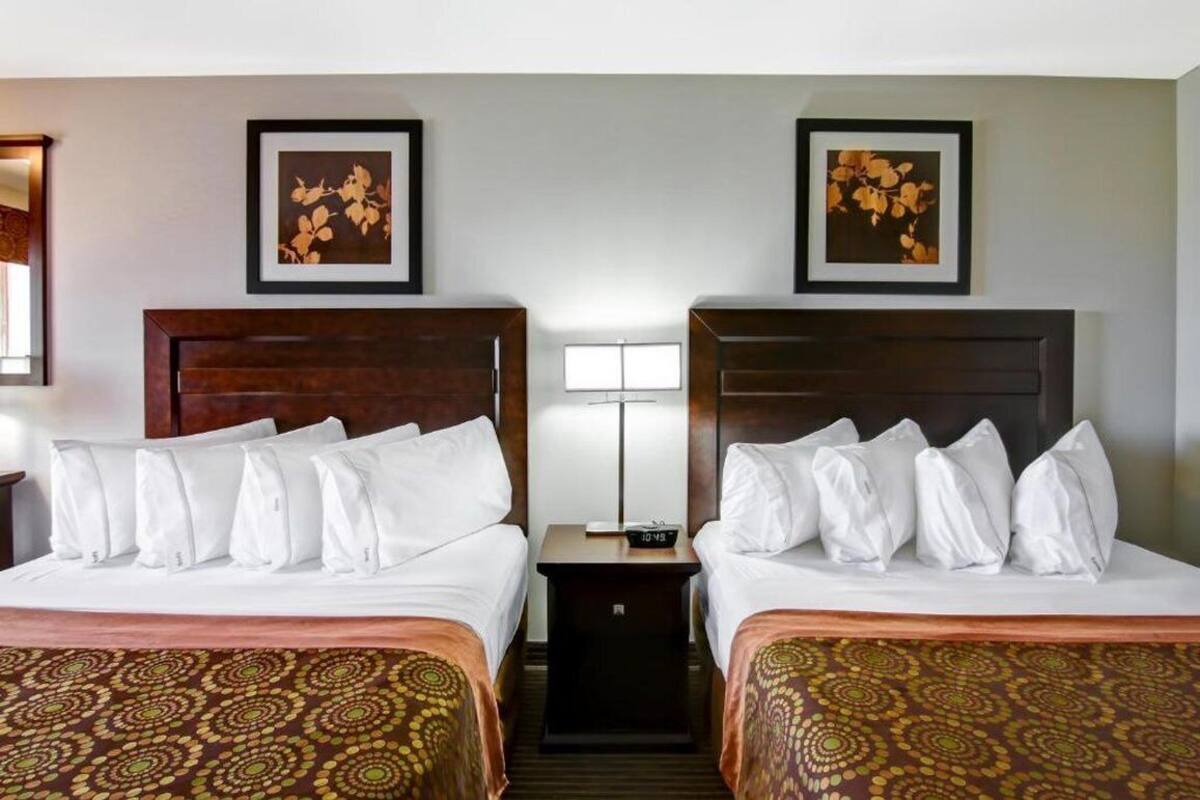 A hotel room with two beds, a nightstand, a lamp, and framed artwork on the wall.