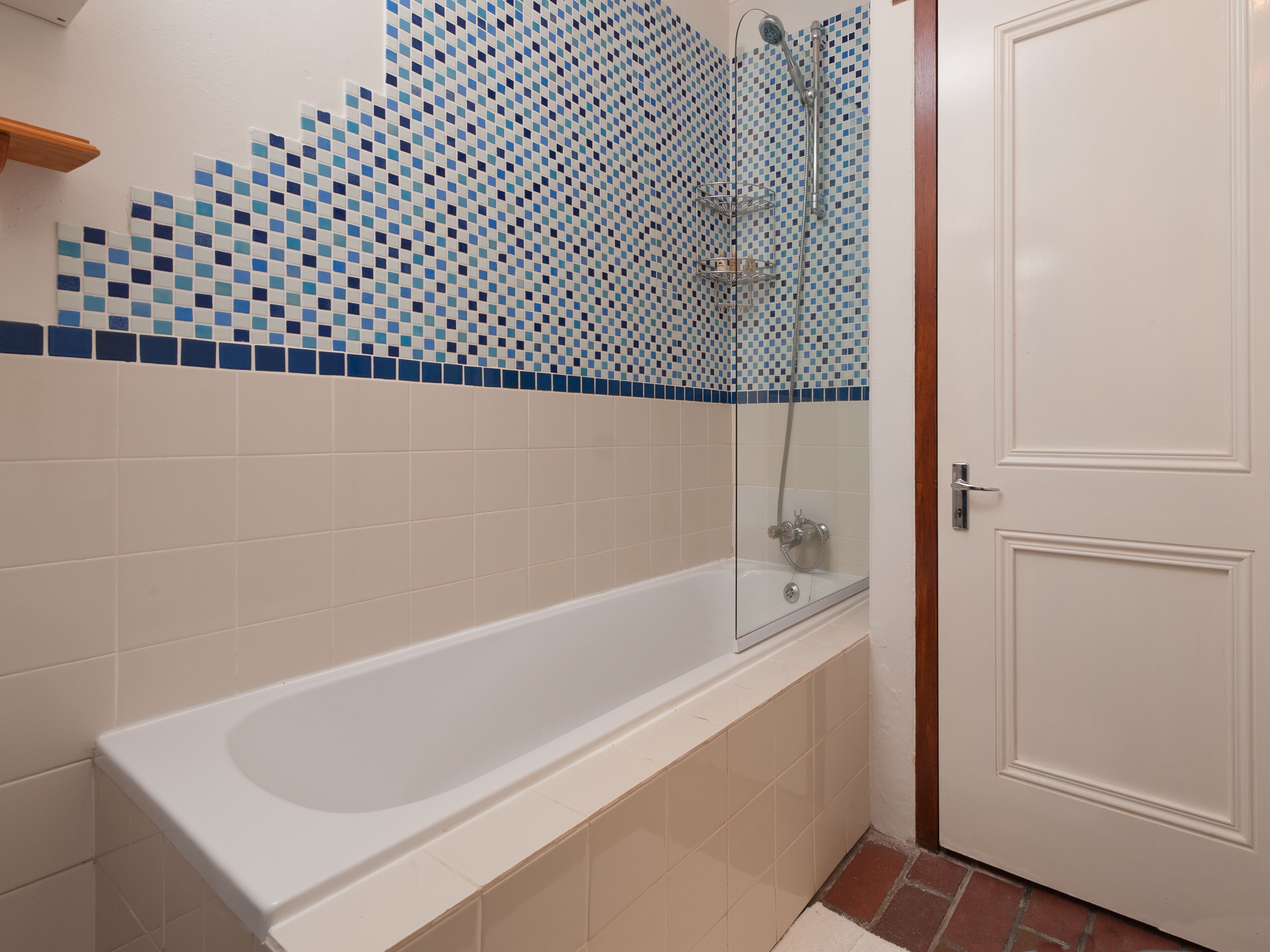 A bathroom with a white bathtub, a shower, and a tiled wall with a blue and white pattern.
