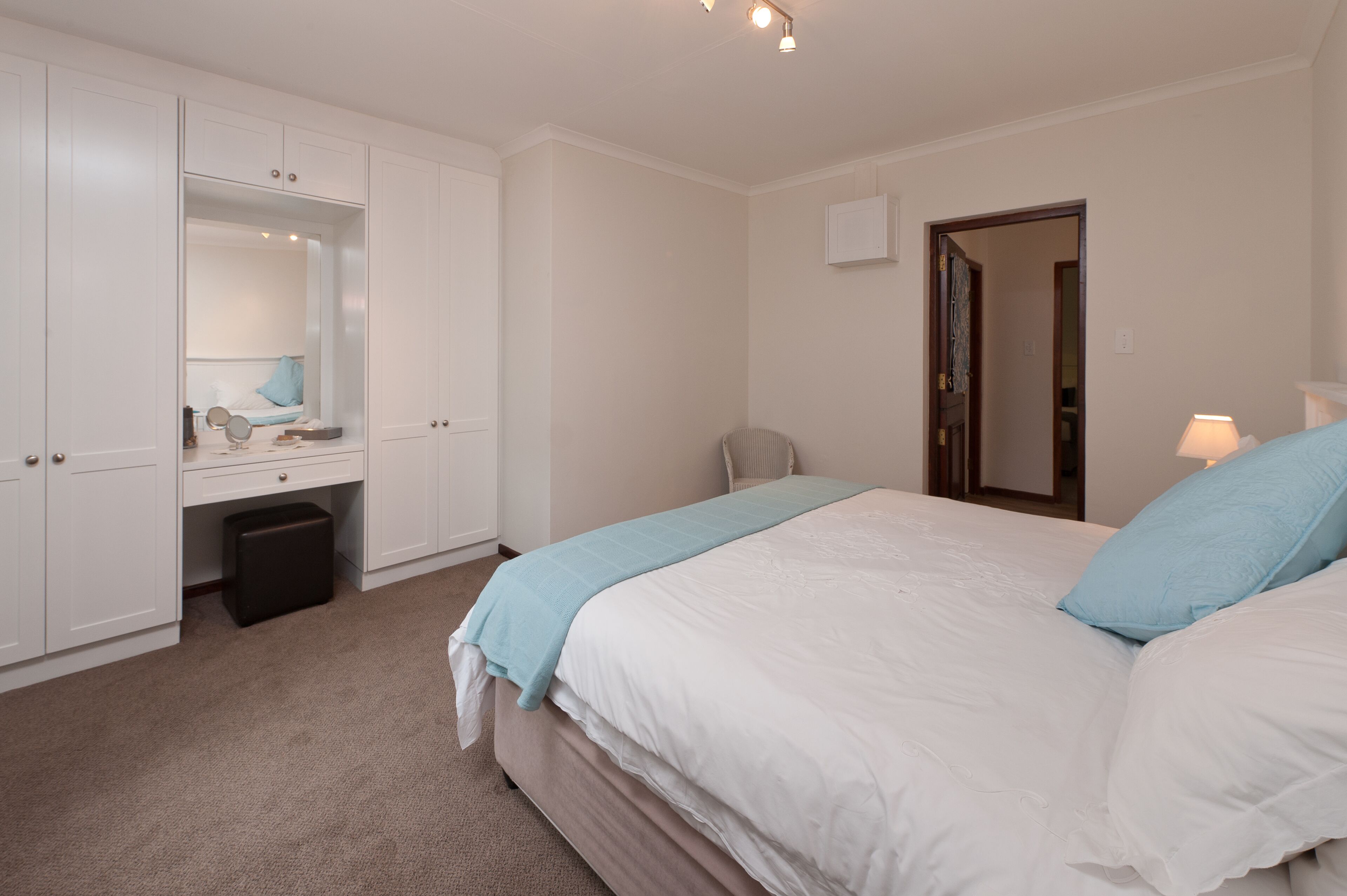 A bedroom with a bed, a desk, a chair, a mirror, and a wardrobe.