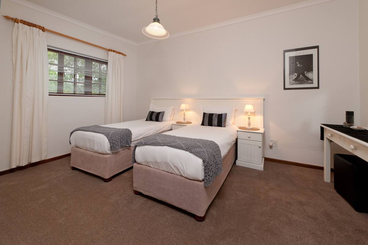 A hotel room with two beds, a desk, a chair, a lamp, and a framed picture on the wall.