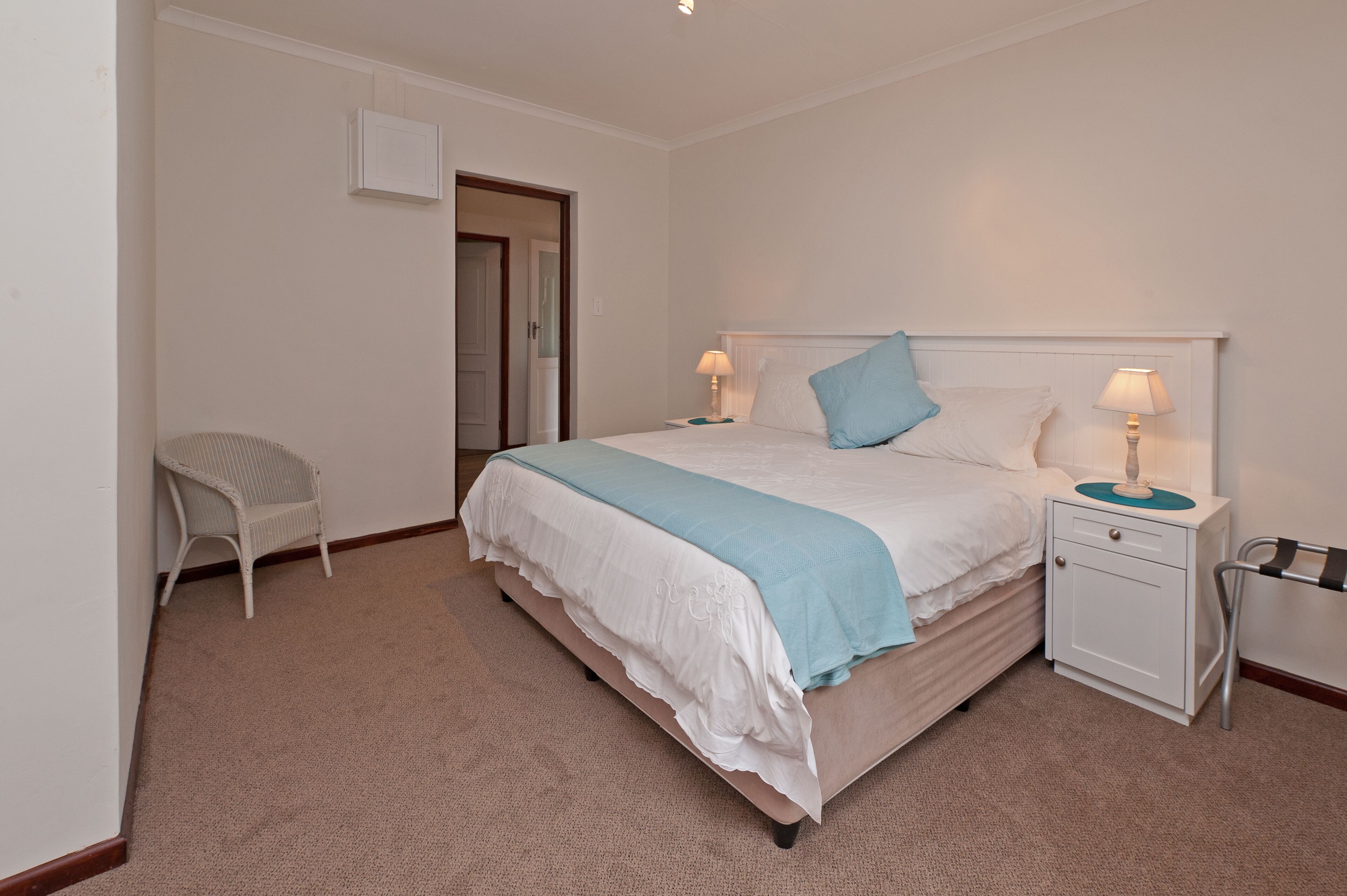 A neatly arranged bedroom with a bed, bedside tables, a chair, and a door.