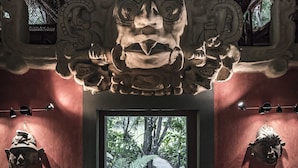 Ein traditionelles Interieur mit einer geschnitzten Holzbalkendecke, einem Steinpfad, der nach draußen führt, und zwei gepolsterten Sitzbereichen.