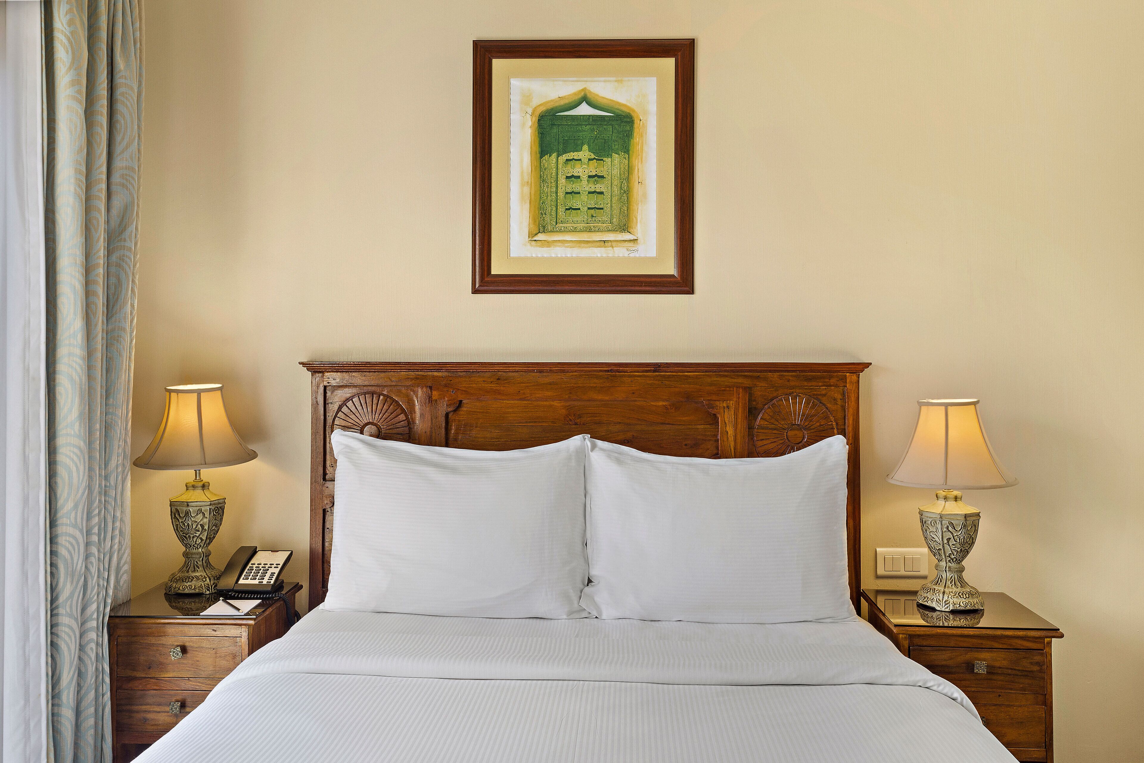A neatly made bed with white linens, two bedside tables with lamps, a wooden headboard, and a framed picture on the wall.