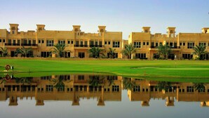 A large, multi-story building with a symmetrical facade, a well-maintained lawn, and a body of water reflecting the structure. - Al Hamra Village Hotel (Ras Al Khaimah)