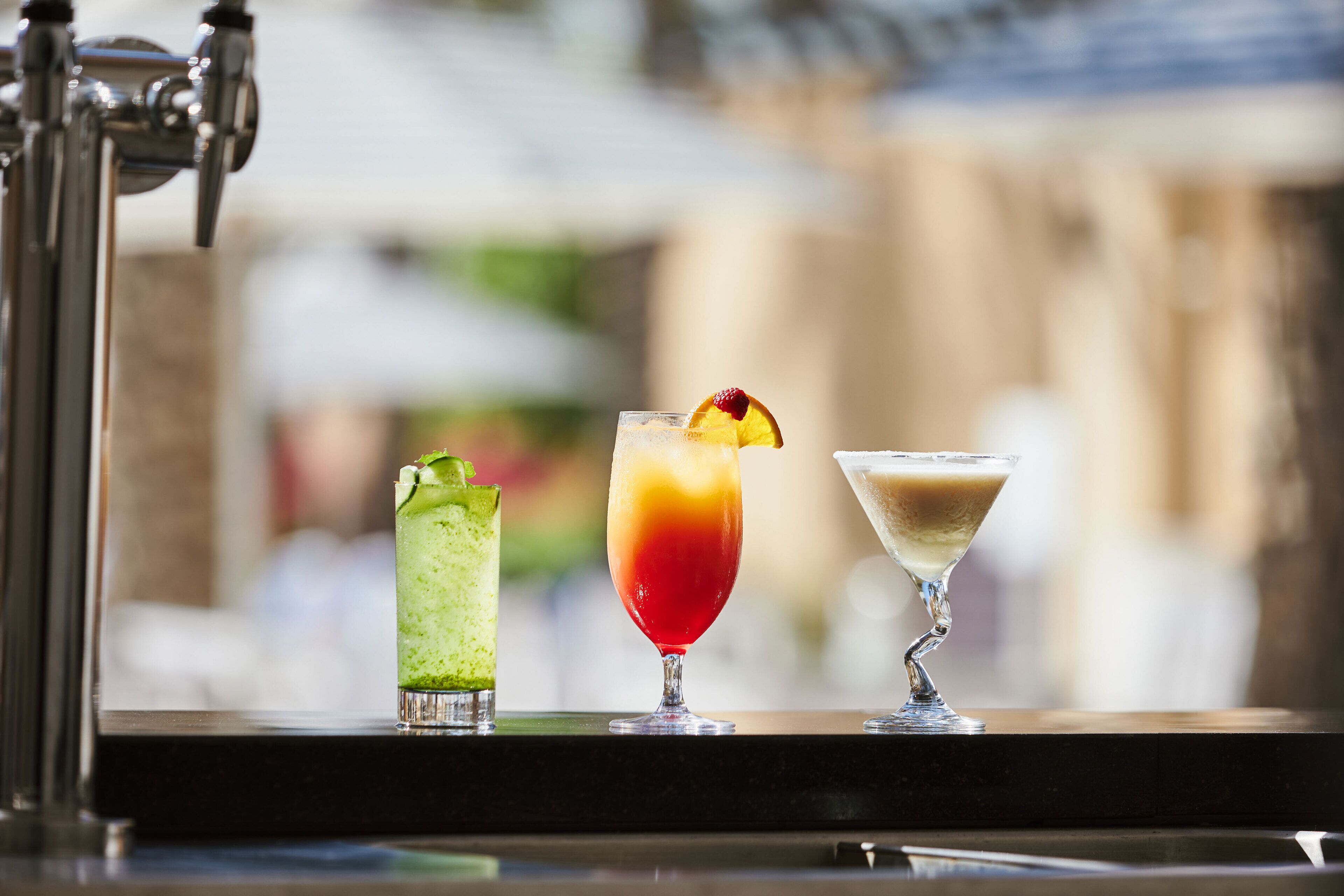 Drei Cocktails auf einer Bar, unscharfer Hintergrund.