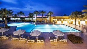 A swimming pool area with lounge chairs and umbrellas, surrounded by palm trees and a building with warm lighting. - Al Hamra Village Hotel (Ras Al Khaimah)