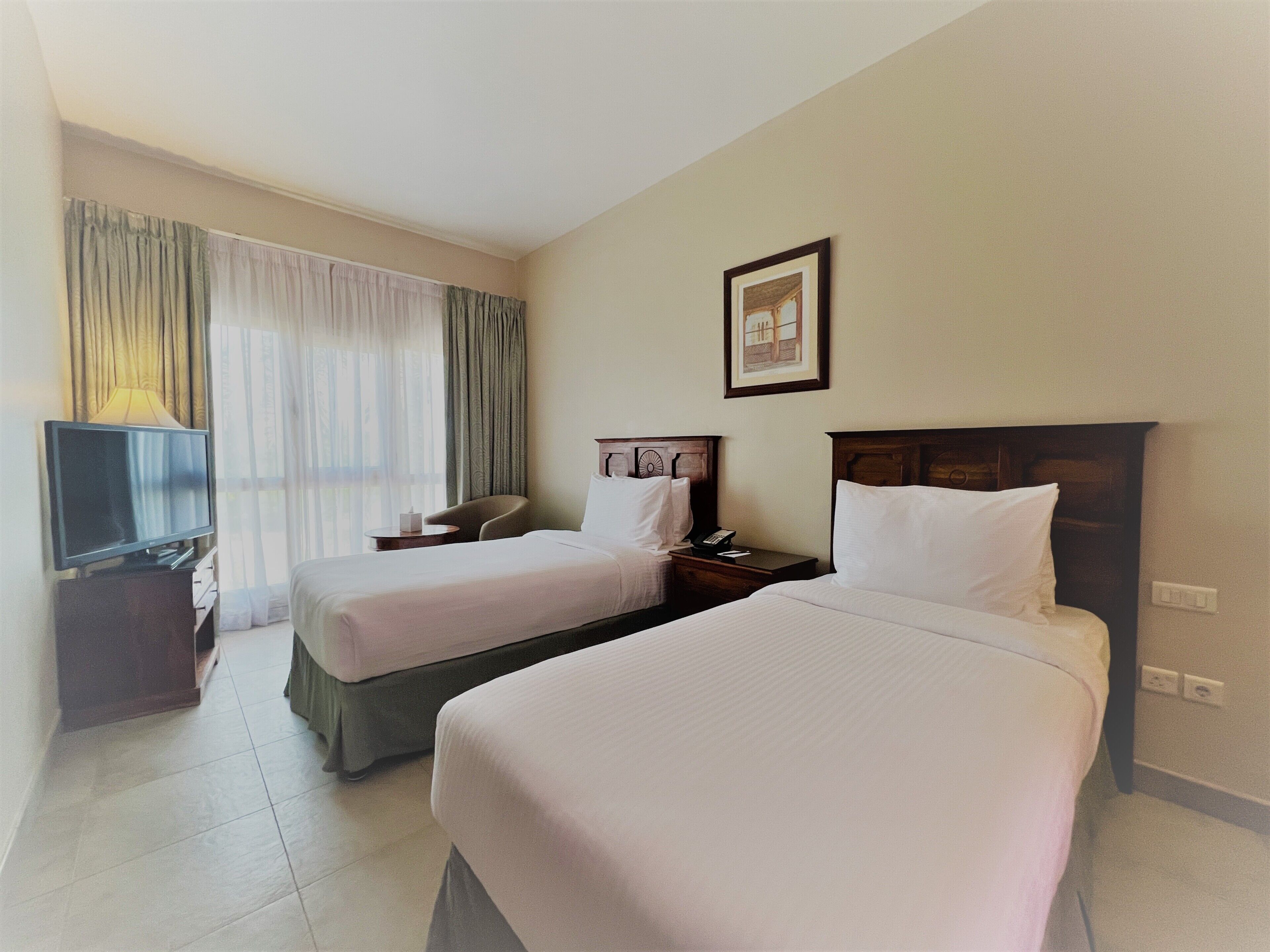 Habitación de hotel con dos camas, televisión, escritorio y ventana con cortinas.