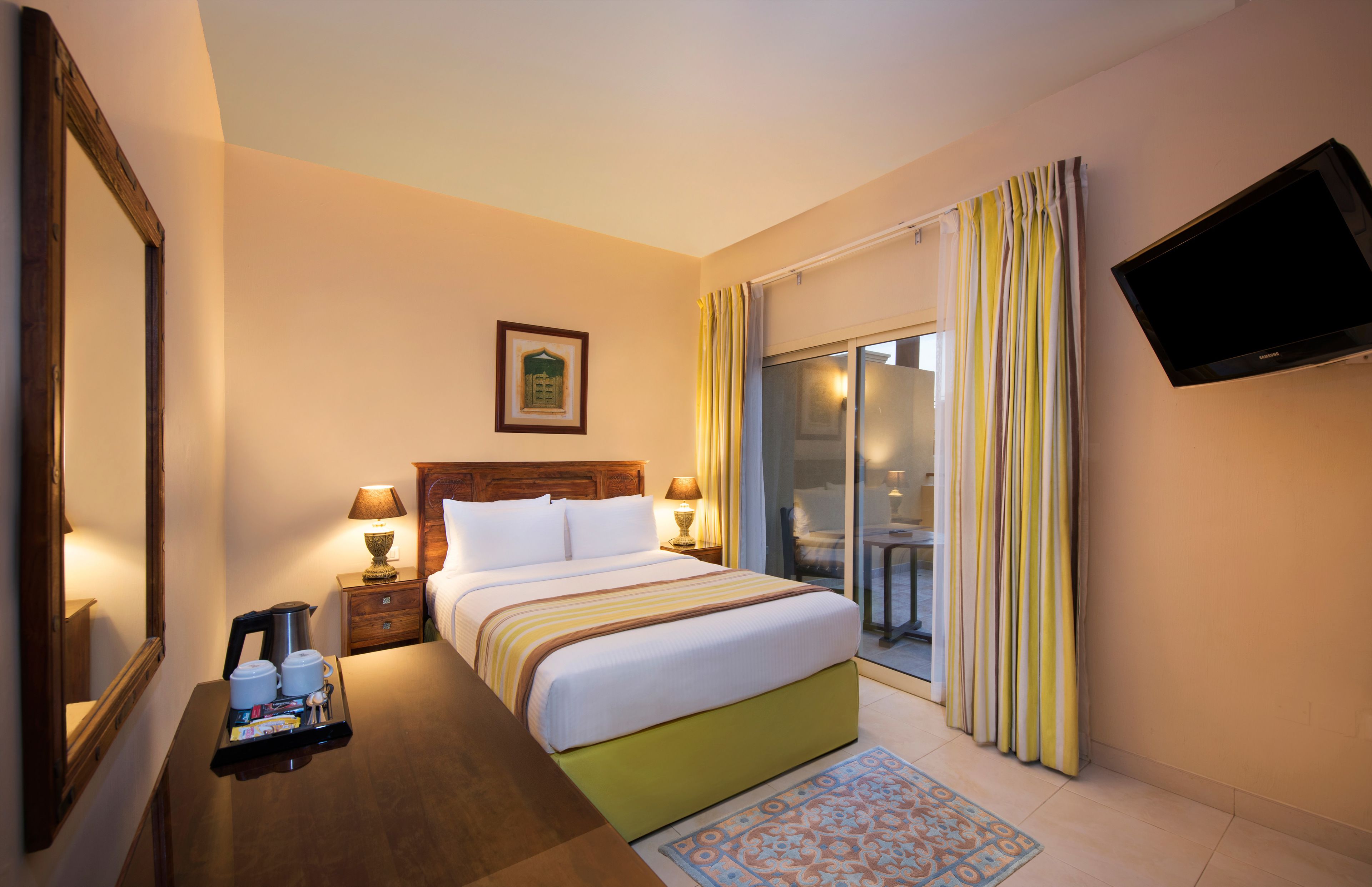 Habitación de hotel con cama, lámparas de noche, televisión, ventana con cortinas y una bandeja con artículos de aseo.