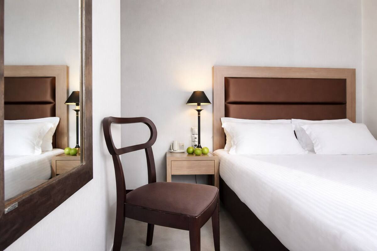 A hotel room with a bed, a chair, a nightstand, a lamp, and a mirror.