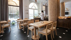 A restaurant with wooden tables and chairs, a buffet area, and a large window with curtains. - Athens Lotus Hotel (Athens)