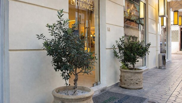 A hotel entrance with a sign reading 'EIZOAOS ENTRANCE,' potted plants, and a tiled walkway. - Athens Lotus Hotel (Athens)
