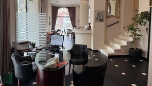 A hotel lobby with a reception desk, a staircase, and a seating area with a glass table. - Athens Lotus Hotel (Athens)