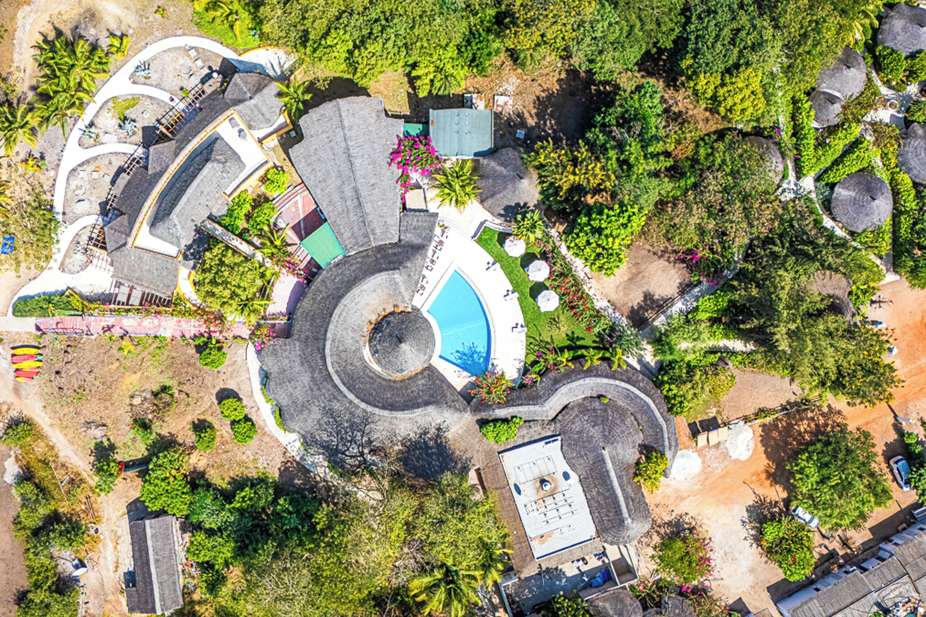 An aerial view of a resort with a central swimming pool, multiple guest areas, and lush landscaping.