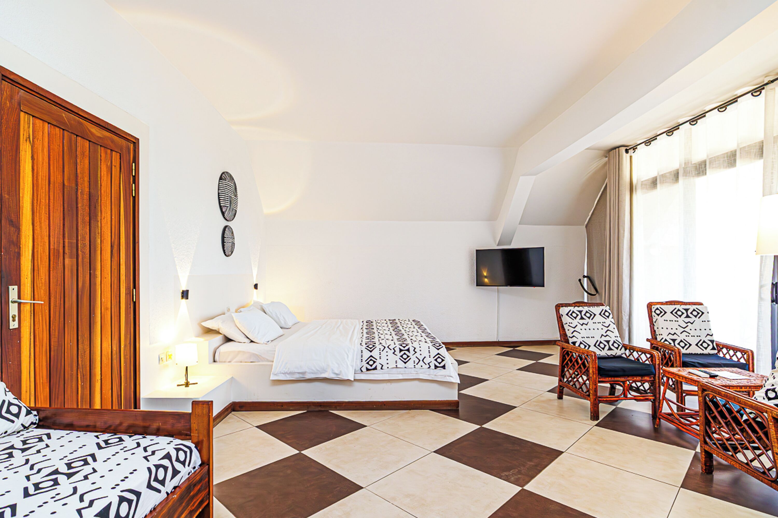 A bedroom with a bed, two chairs, a TV, and a wooden door.