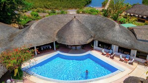 Una piscina con estructura de techo de paja, rodeada de sillas de descanso y plantas en macetas.