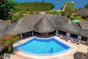 A swimming pool with a thatched roof structure, surrounded by lounge chairs and potted plants.