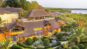 Un resort con varias construcciones de techo de paja, un jardín cuidado y vistas al agua.