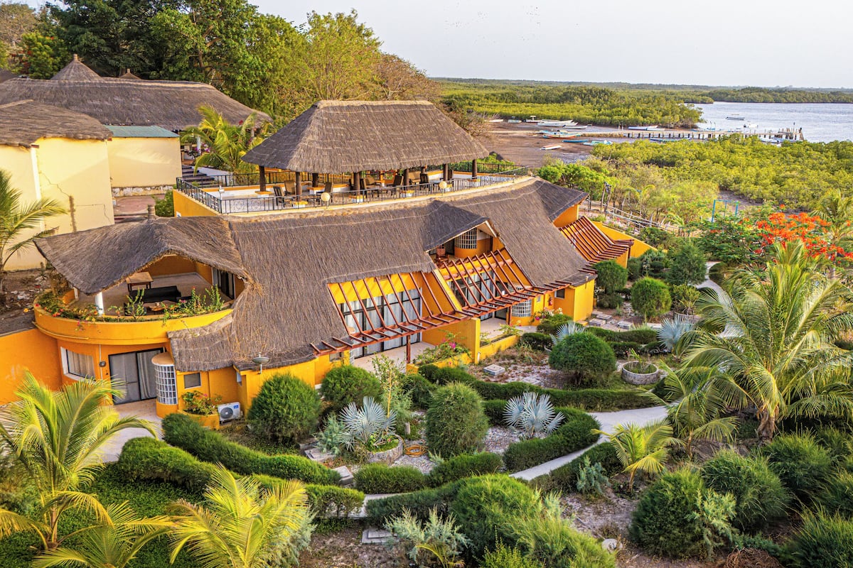 A resort with multiple thatched-roof structures, a well-maintained garden, and a view of the water.