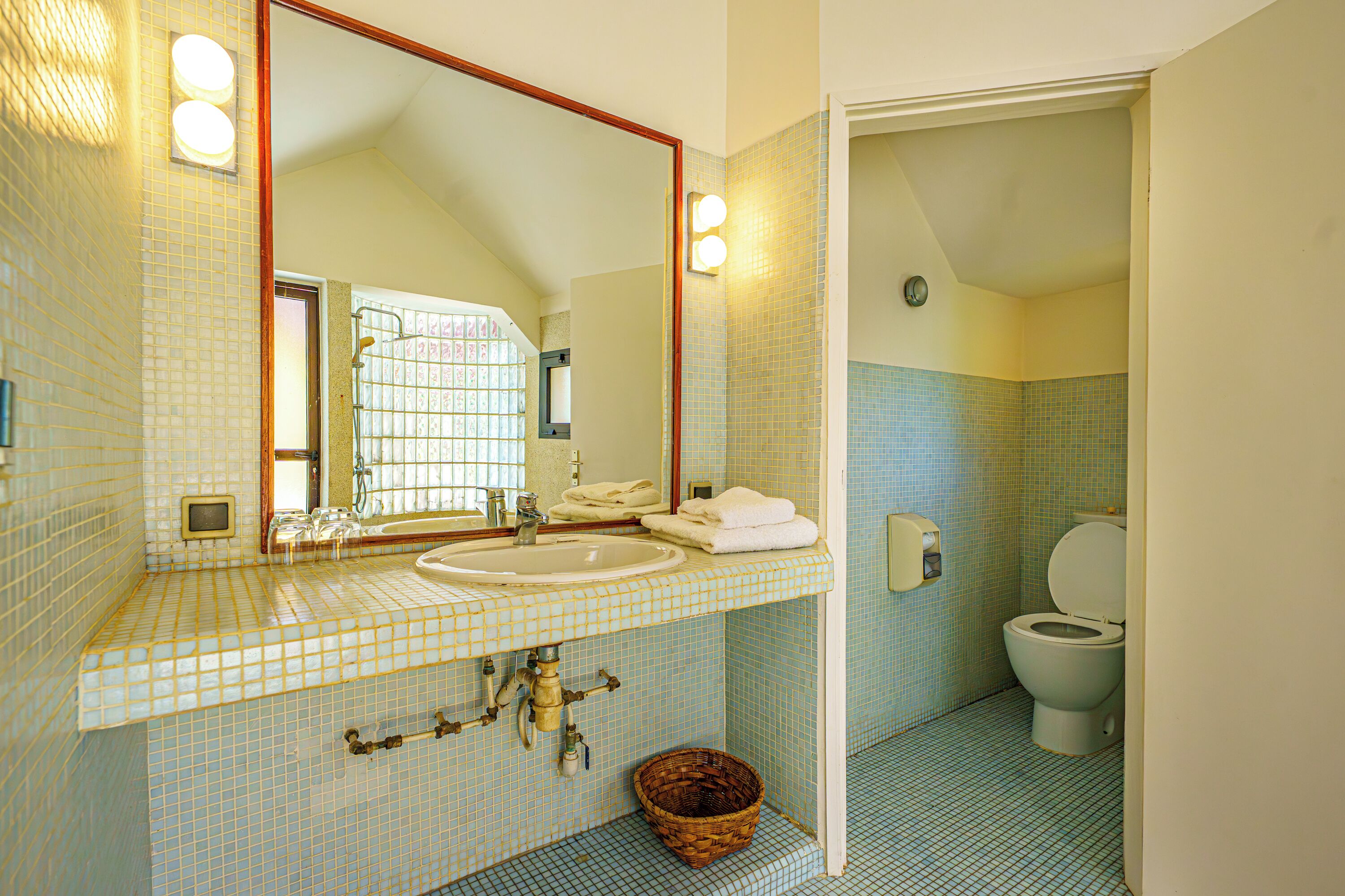 A bathroom with a tiled floor, a sink with a mirror above it, a toilet, and a basket on the floor.