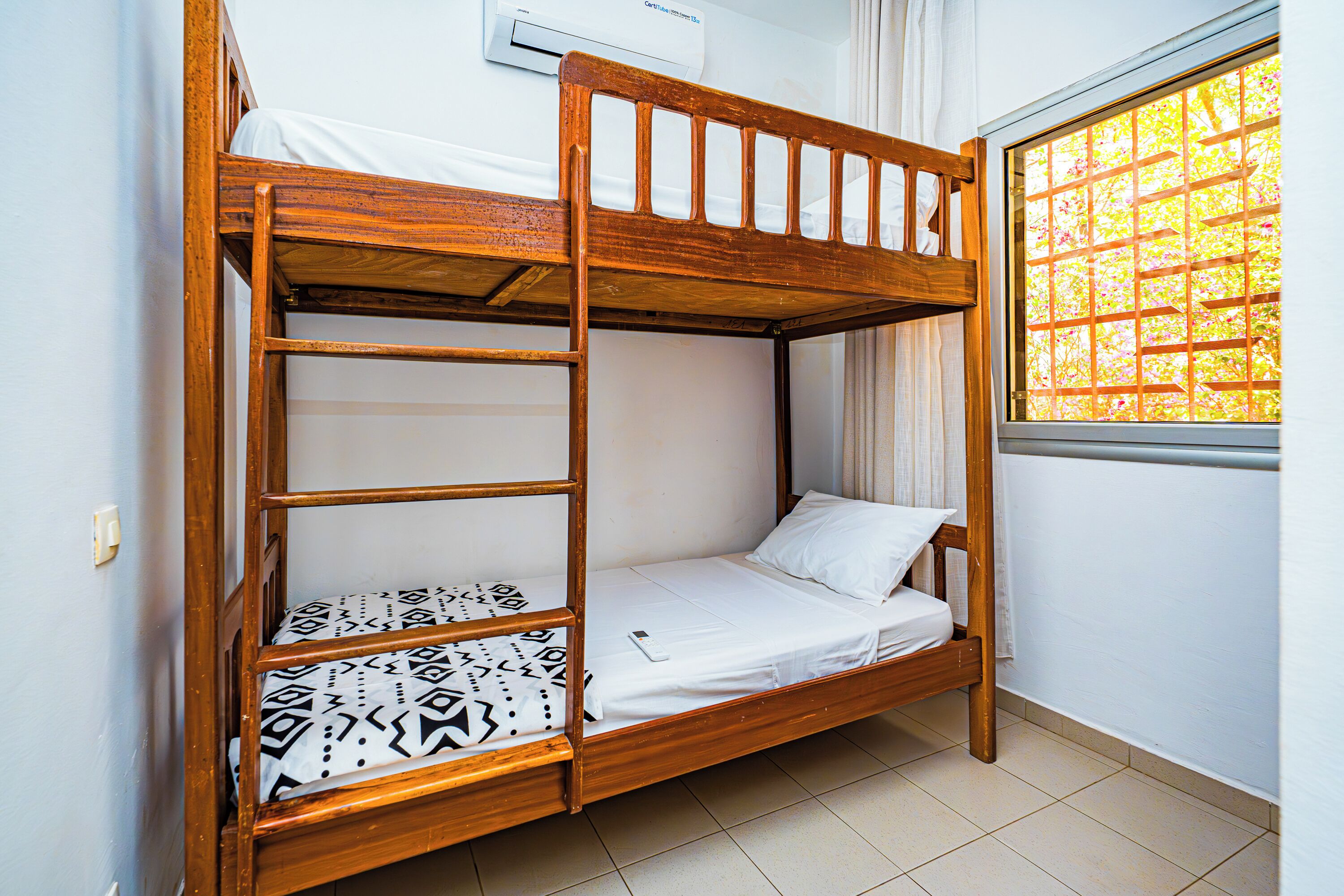 Ein Stockbett mit Holzrahmen, weißer Bettwäsche und einem gemusterten Kopfkissen.