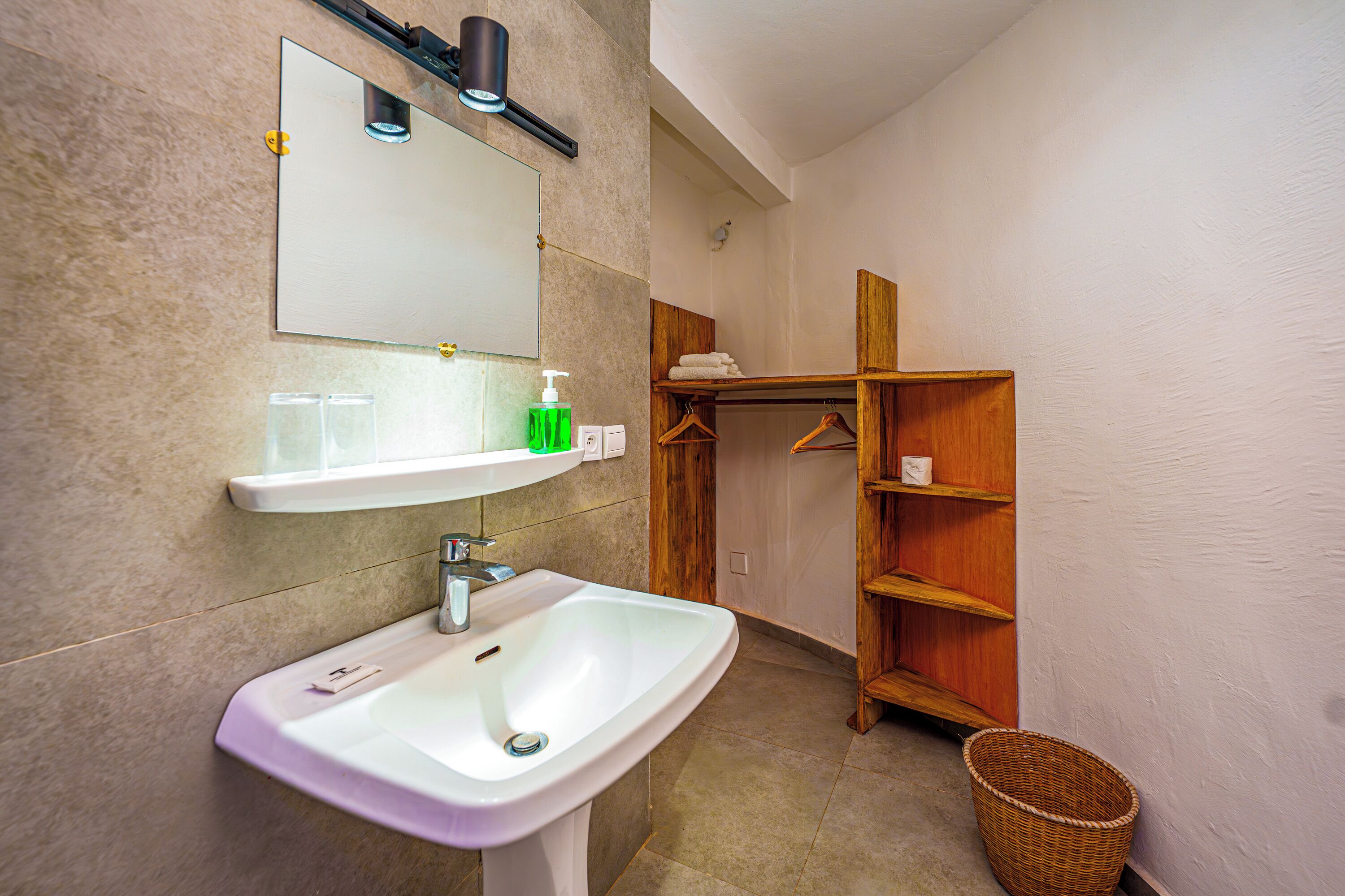 Un baño con un lavamanos blanco, un espejo y estantes de madera.