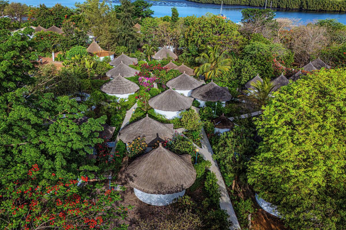 A resort with thatched-roof huts surrounded by lush greenery and a view of the sea.