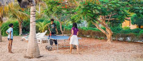 A beach setting with a table tennis table, palm trees, and a few people.