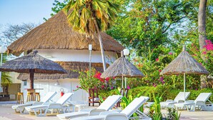 Un resort con cabañas de techo de paja, sillas de descanso blancas y una zona de piscina.