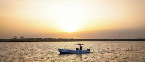 A boat with the text "KEUR SALOM" and "SUI MANGA" on its side, floating on calm water during sunset.