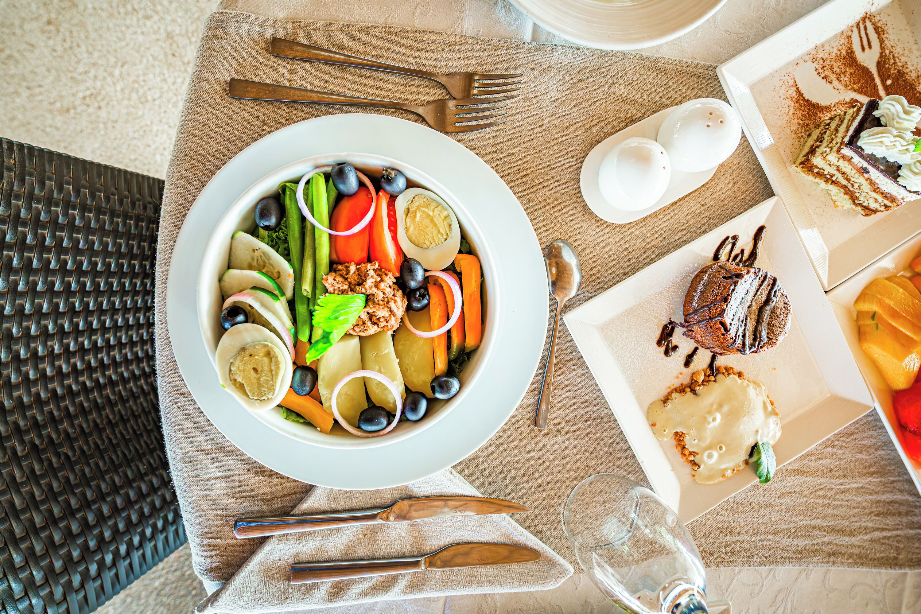 Ein Tisch mit einer Salatschüssel, einem Kuchenteller und einem Glas Wasser.