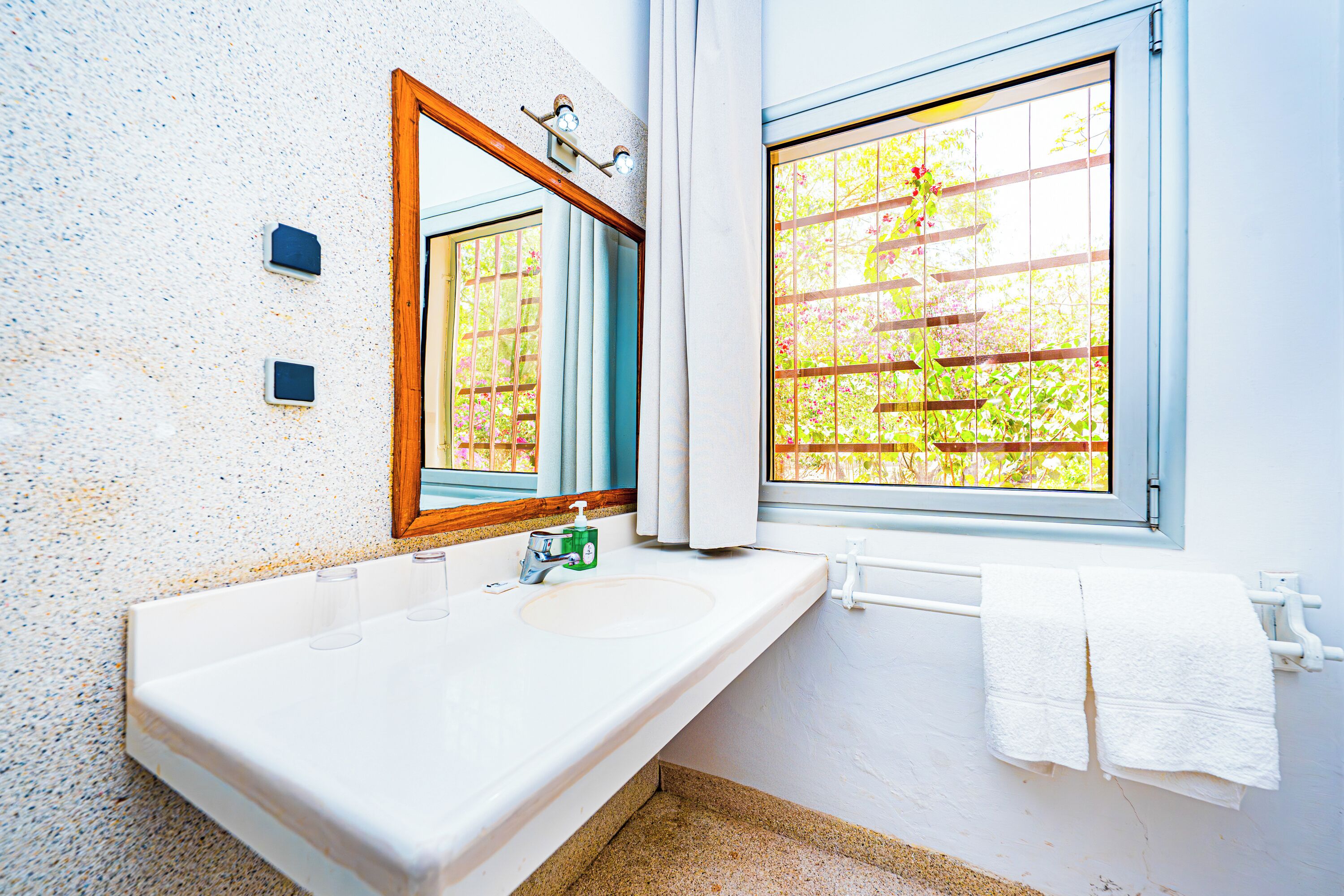 Un bagno con un lavandino bianco, uno specchio e una finestra vista verde.
