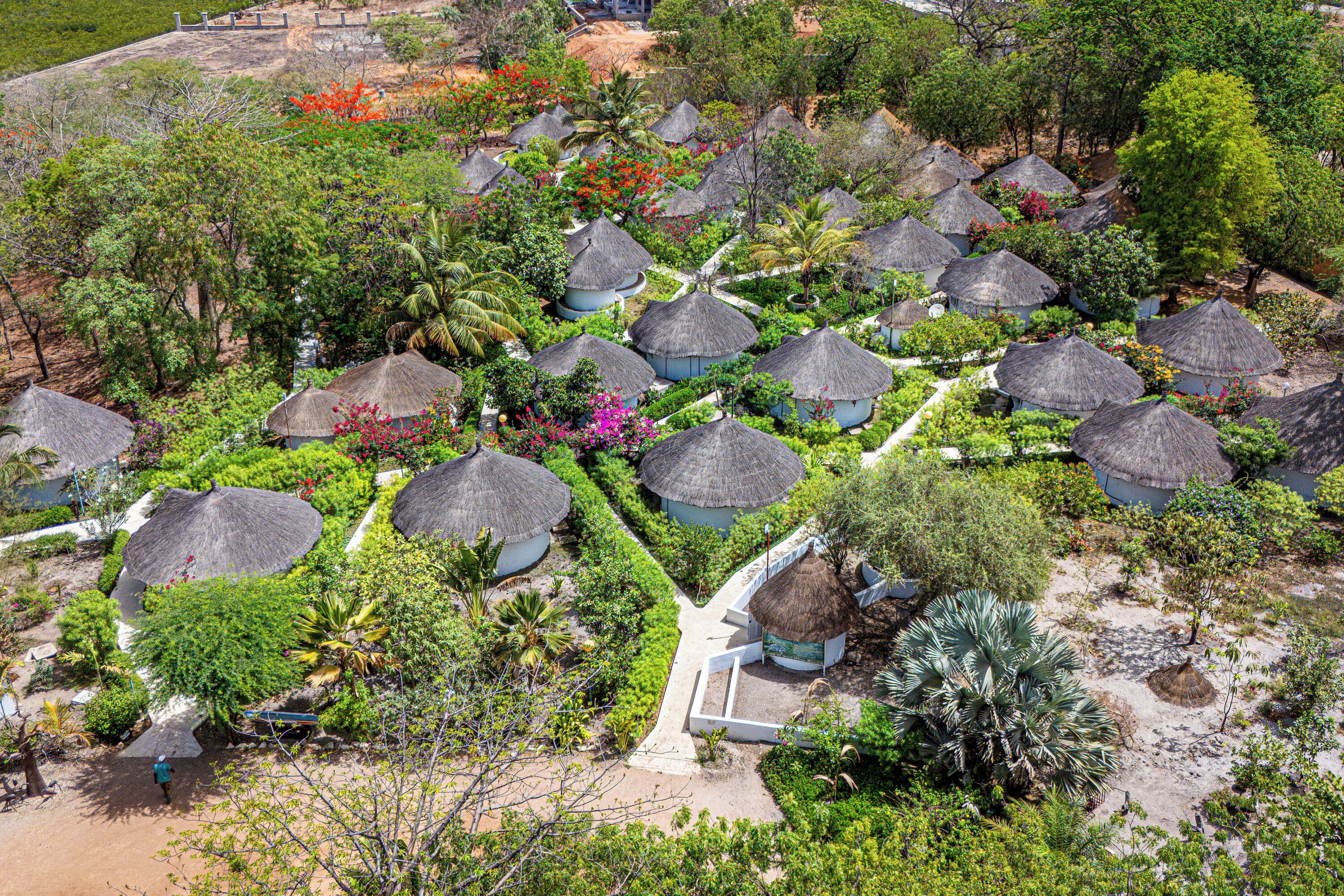 An aerial view of a resort with thatched-roof huts arranged in a garden setting.