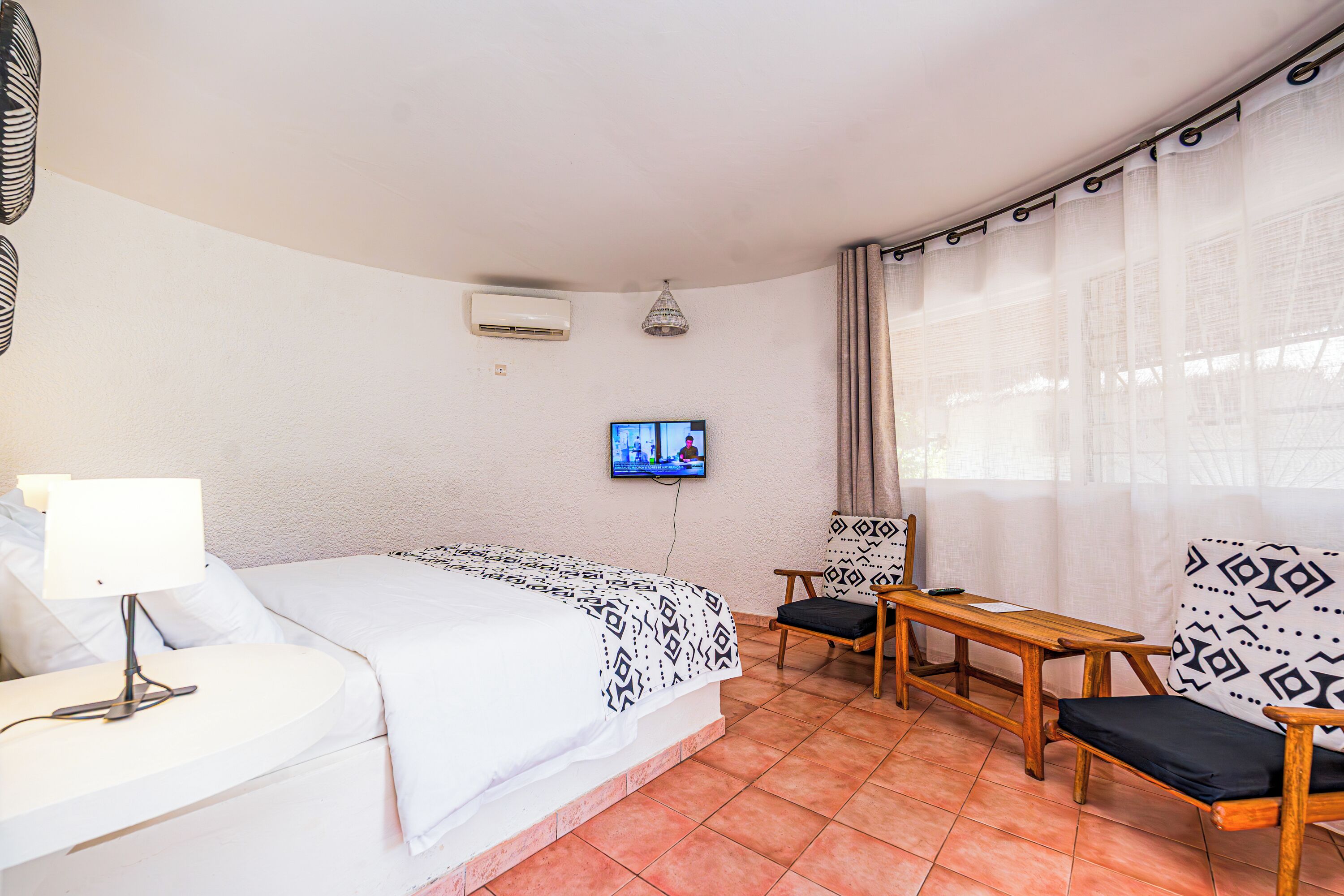 A hotel room with a bed, a desk, a chair, a TV, and a window with curtains.