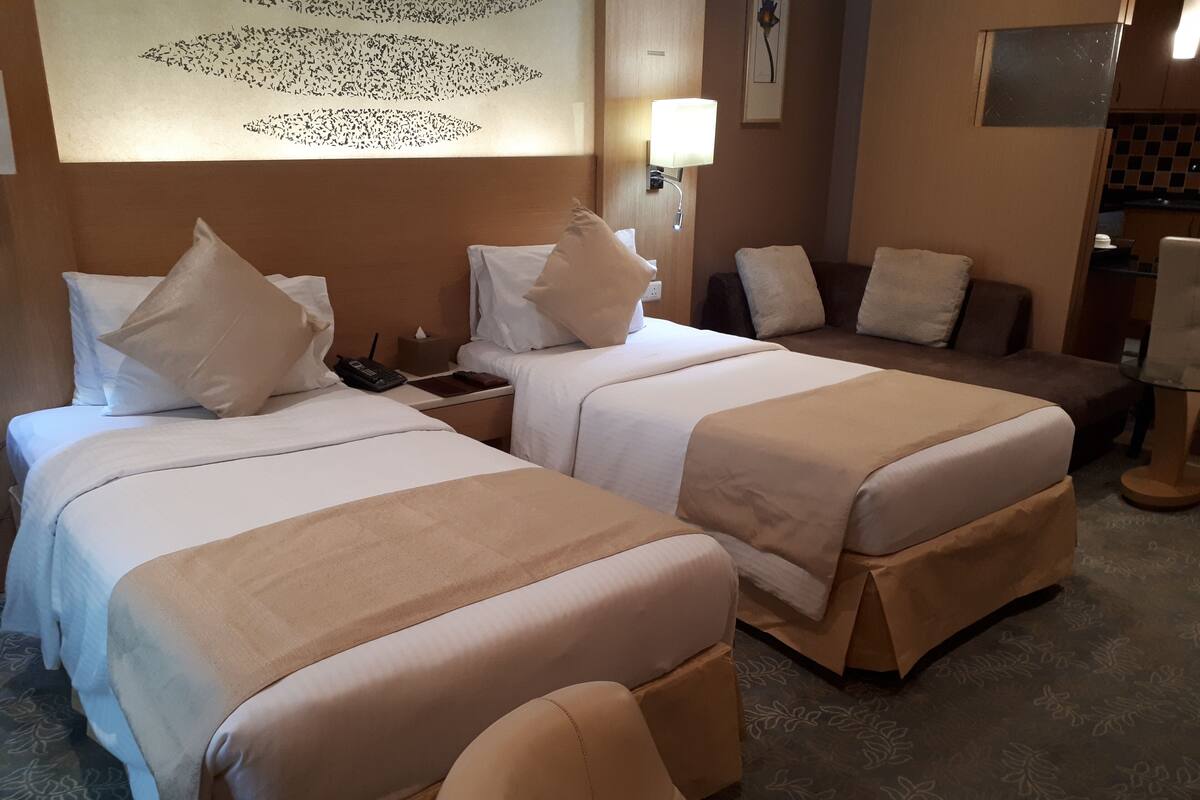 A hotel room with two beds, a nightstand, a desk, a chair, and a wall-mounted lamp.