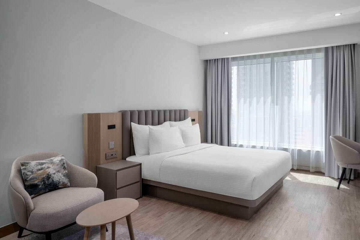 A modern hotel room with a large bed, a bedside table, a chair, and a small table.