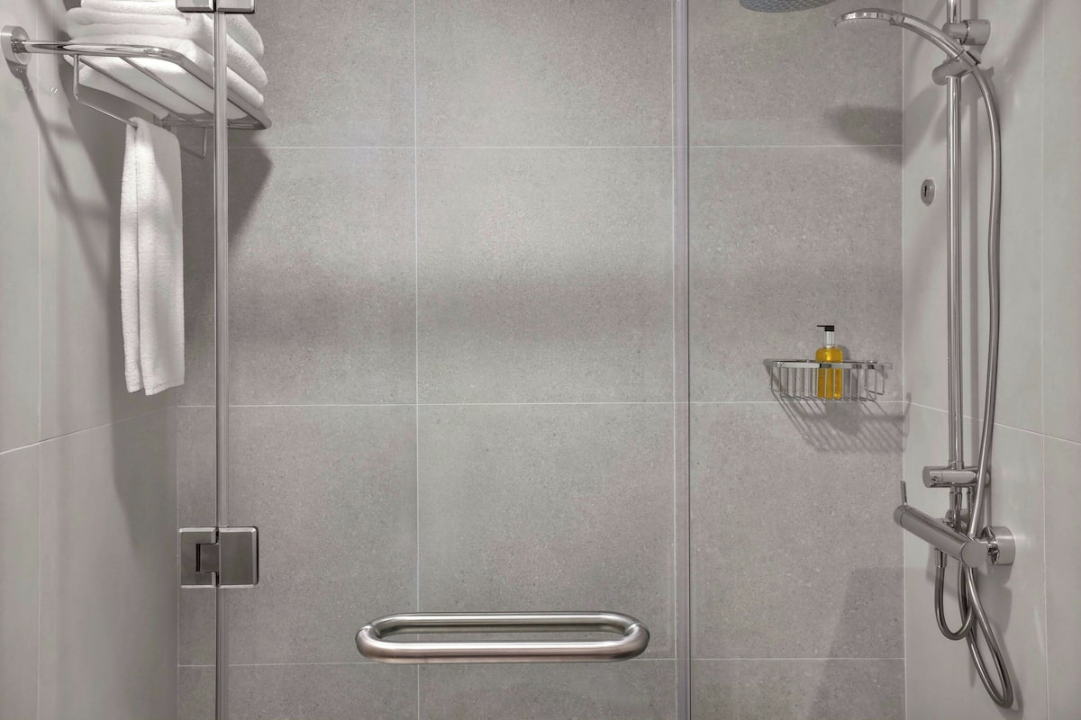 A modern shower area with a glass door, a towel rack with towels, a soap dispenser, and a grab bar.
