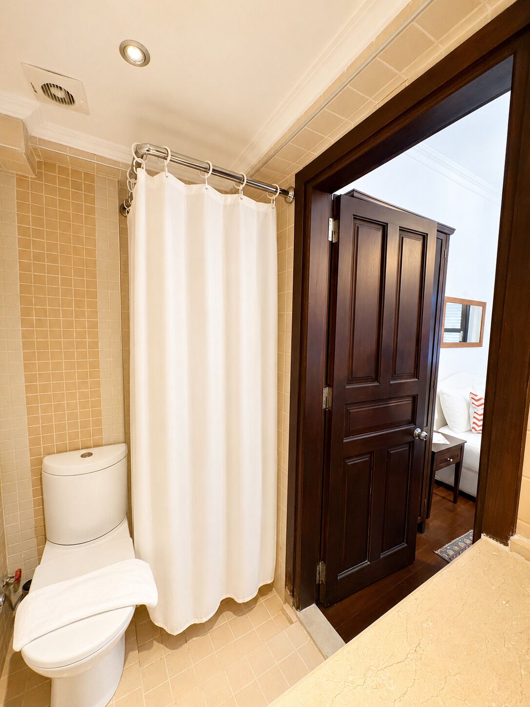 A bathroom with a toilet, a shower curtain, and a wooden door leading to a bedroom.