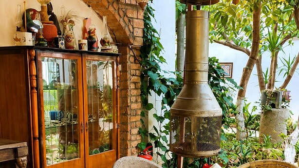 A dining area with a brick wall, a large chimney, wicker chairs, and a table set with plates and food.