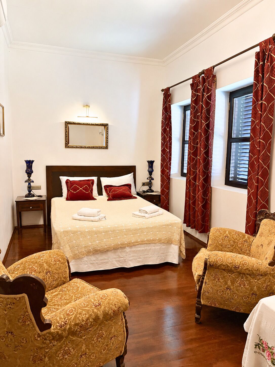 Habitación de hotel con una cama grande, dos mesitas de noche, un espejo, una ventana con cortinas y dos sillones estampados.