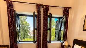 A hotel room with a large bed, a nightstand, a chair, and a window with curtains.