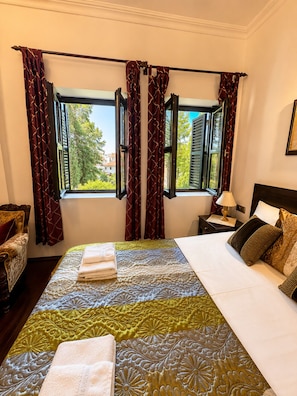 A hotel room with a large bed, a nightstand, a chair, and a window with curtains.