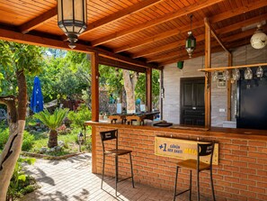 Un espace bar extérieur abrité, avec des murs en briques, un plafond en bois et des luminaires suspendus.