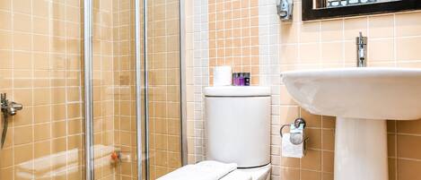 A bathroom with a glass shower enclosure, a toilet, a sink, and a mirror.