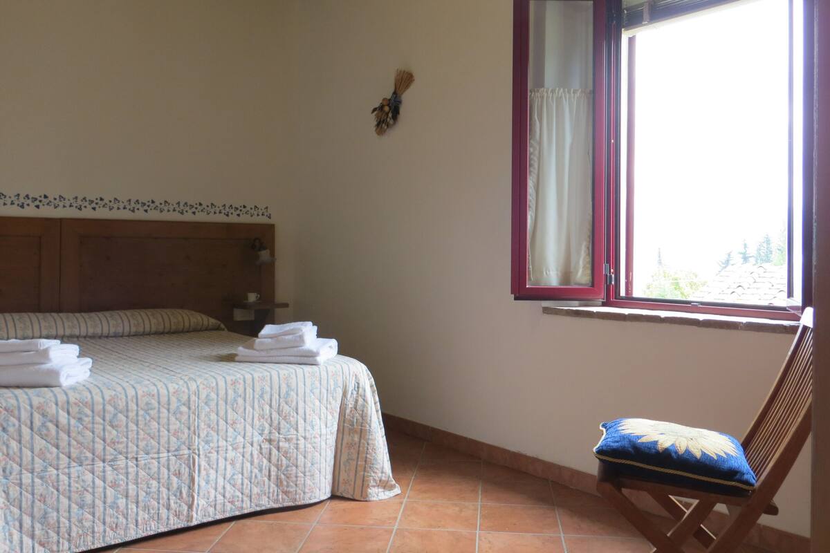 Un dormitorio con cama, una silla, un ventanal con cortinas y un adorno en la pared.