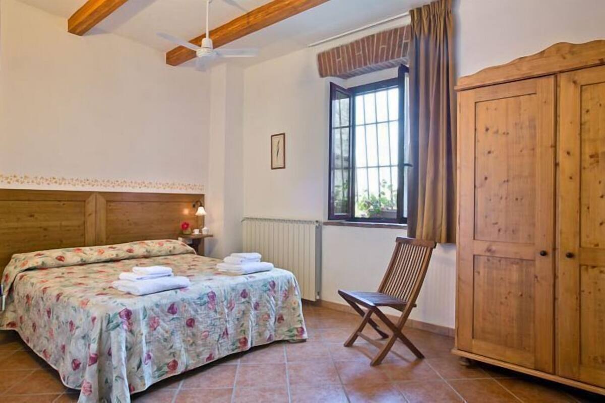 Un dormitorio con cama, una silla, un armario y una ventana con cortinas.